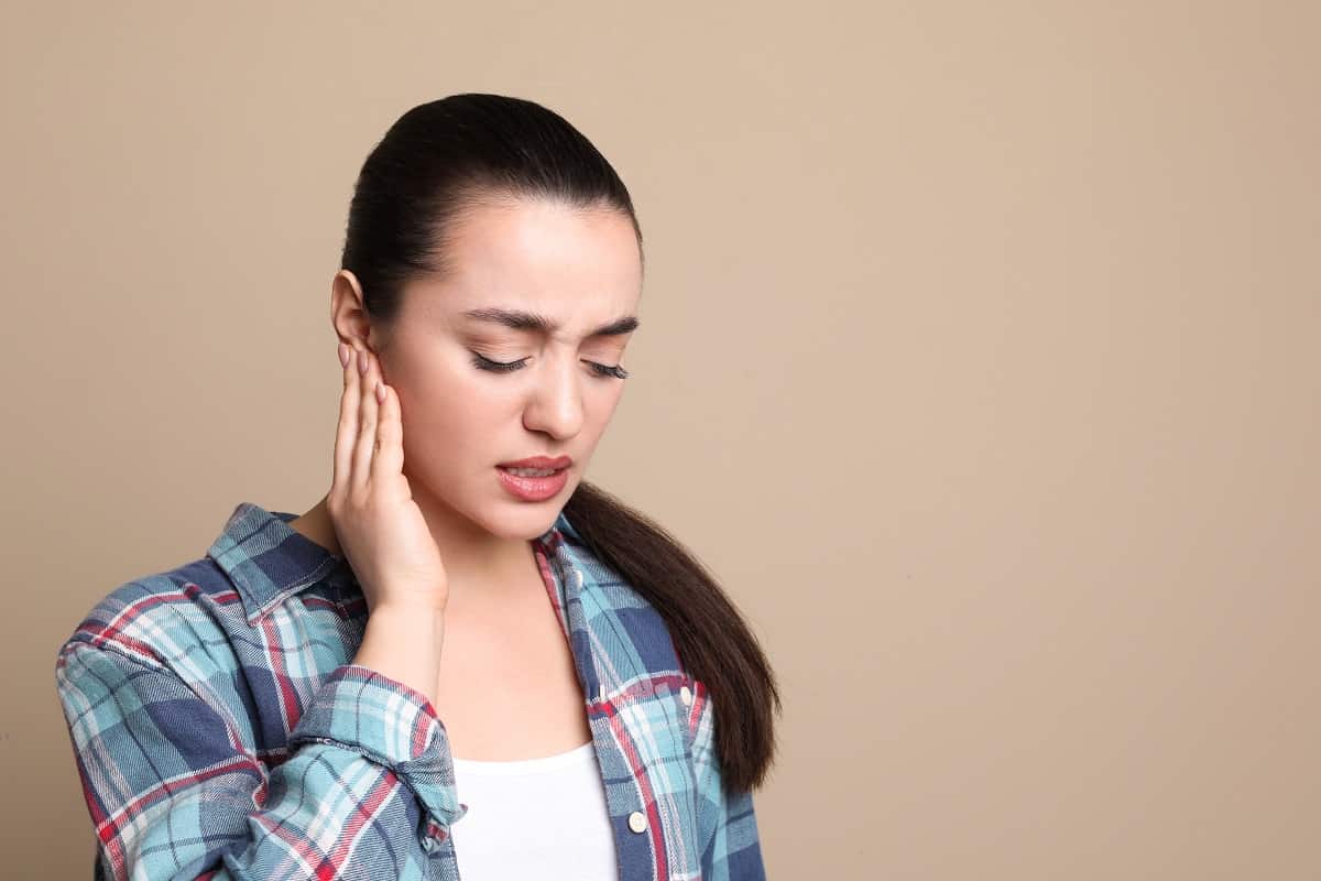 Young Woman Suffering From Ear Pain On Beige Background. Space F